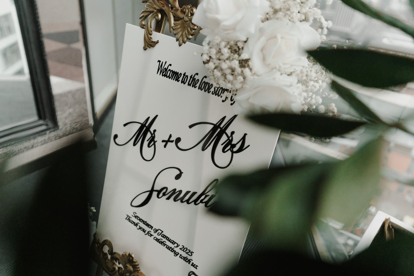 White acrylic Mr and Mrs welcome sign on a gold easel with white roses